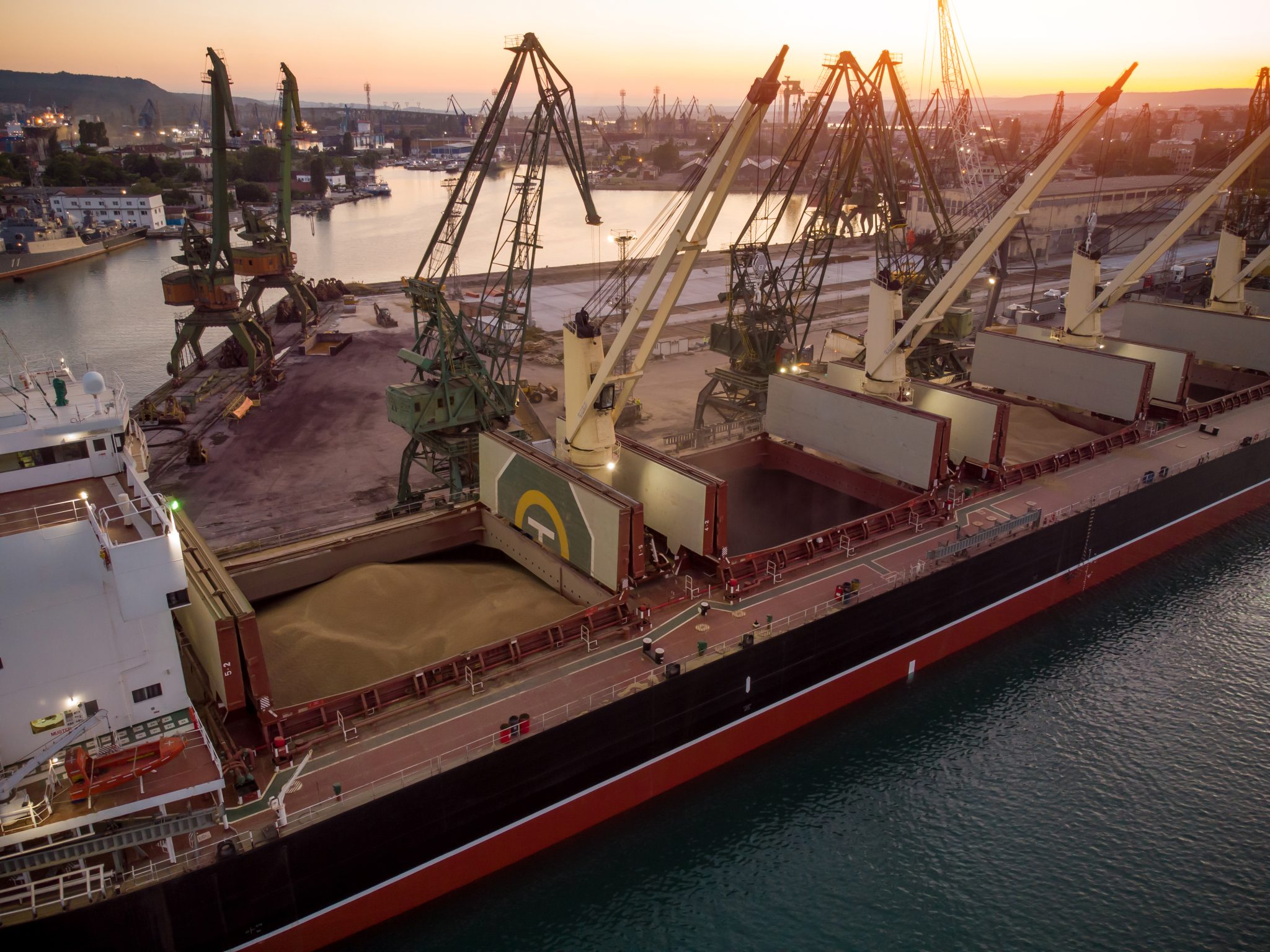 Aerial top view of big cargo ship bulk carrier is loaded with grain of wheat in port at sunset