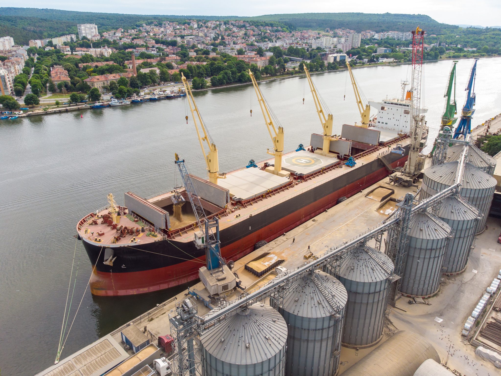 Loading grain into holds of sea cargo vessel in seaport from silos of grain storage. Bunkering of dry cargo ship with grain. Aerial top view
